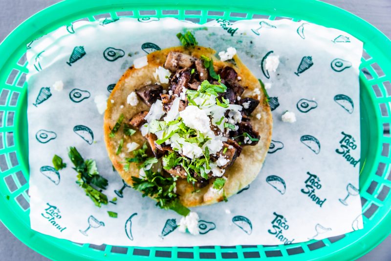 Beef taco topped with cilantro, onions, and crumbled cheese on a soft tortilla in a bright green basket.