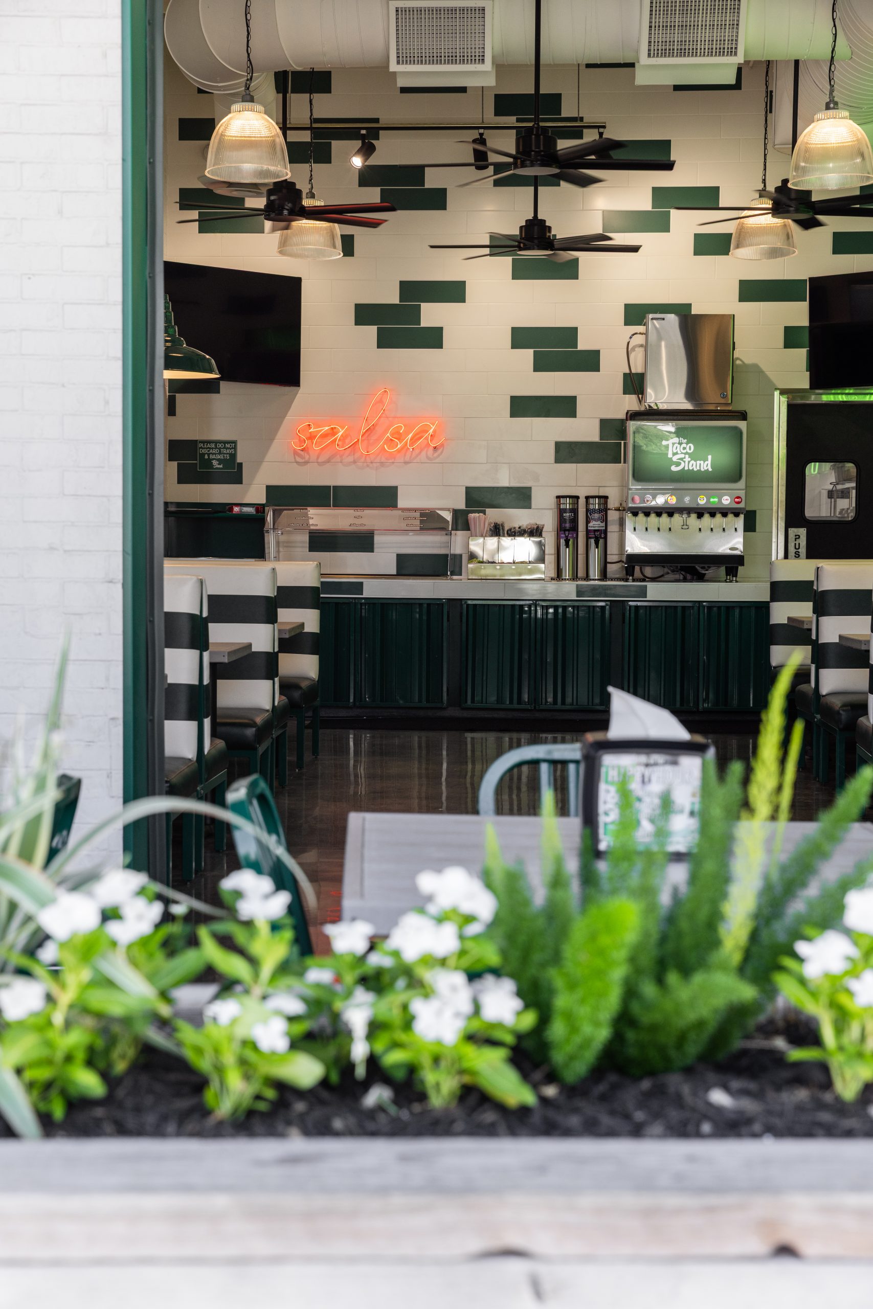 Interior view of a salsa restaurant counter with a neon 'salsa' sign, green and white tiled wall, and beverage dispenser.