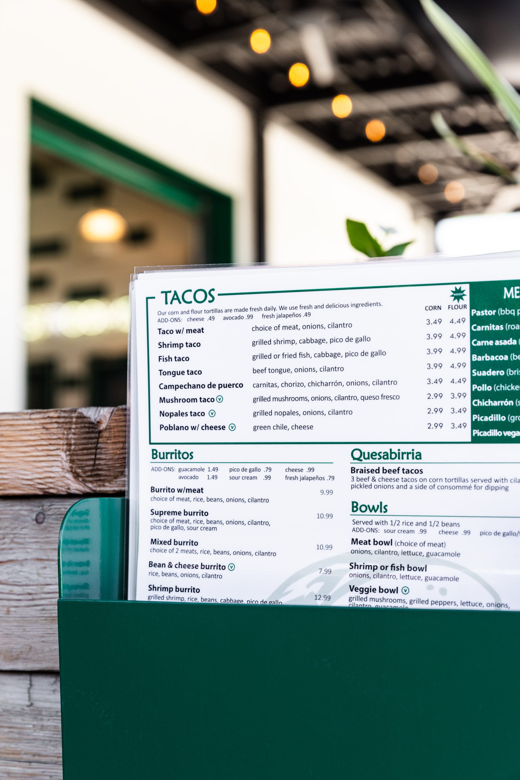 Restaurant menu board featuring tacos and burritos, green border, on a wooden counter