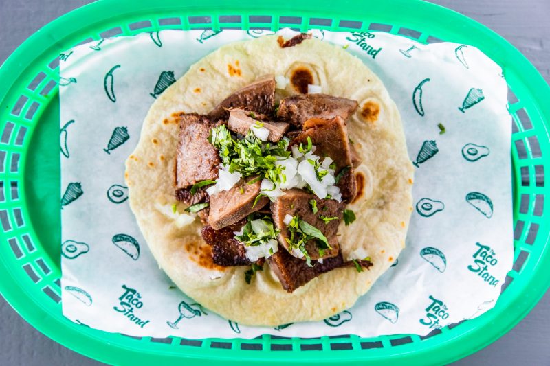 Taco filled with grilled steak, chopped onions, and cilantro in a soft tortilla on a green basket liner.